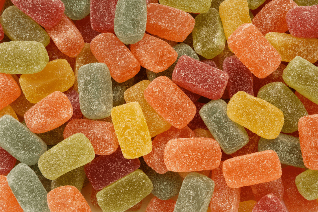 An assortment of colorful THC gummy candies in various shapes and sizes, featuring shades of red, green, orange, and yellow, with a sugar coating giving them a sparkling appearance.